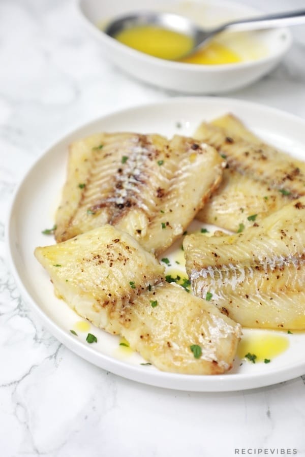 Cooked Cod fillets in a plate topped with garlic butter sauce.