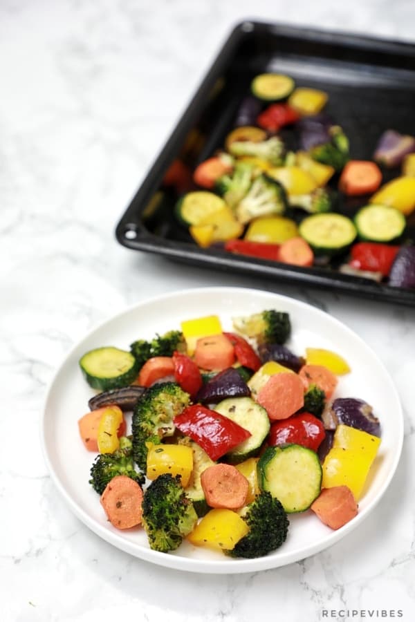 Roasted veggies served on a plate with some still in the baking sheet.
