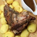 The roasted lamb served on a platter with gravy and potatoes.