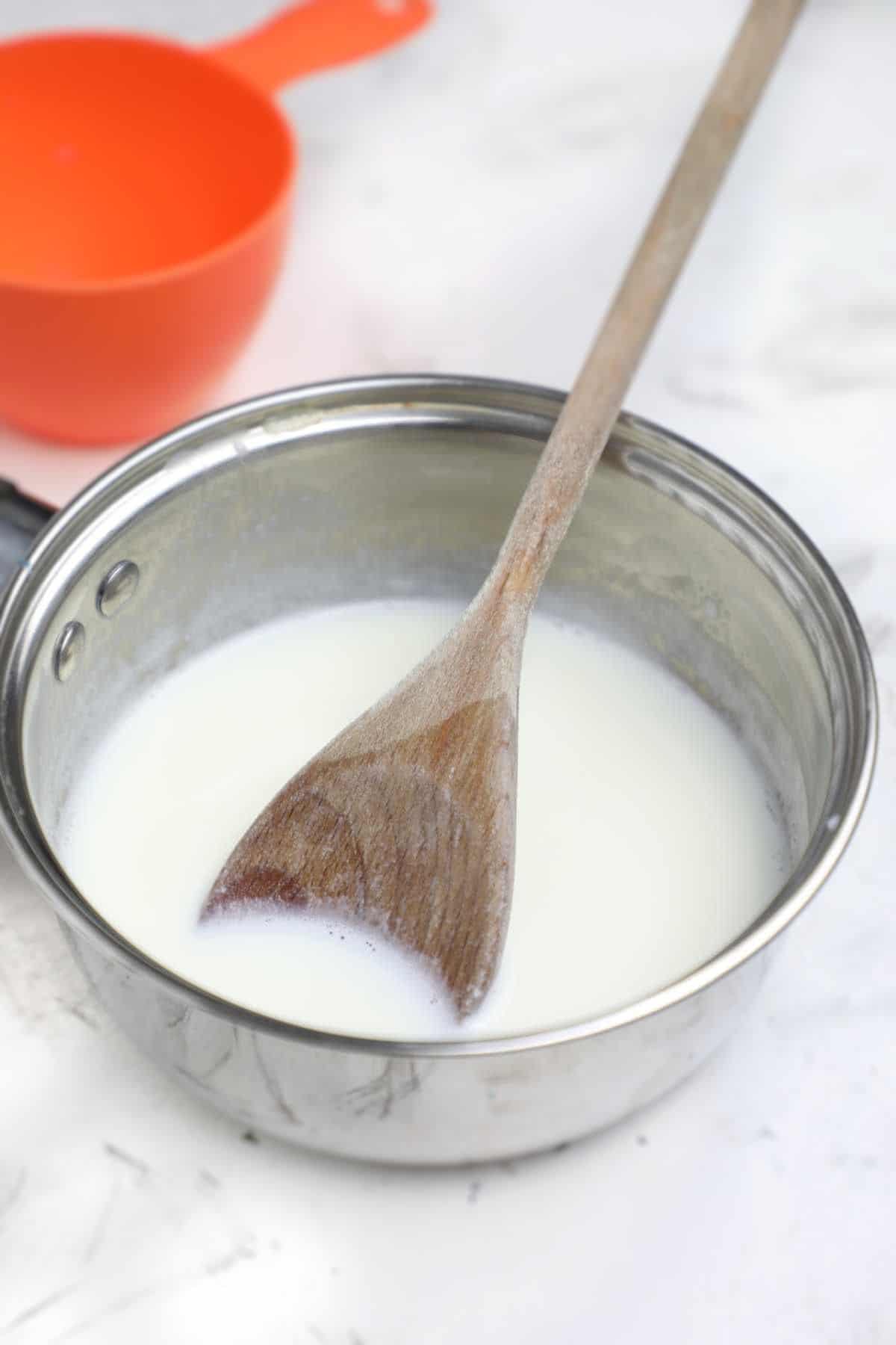 the milk in a pot with a wooden spoon inserted.