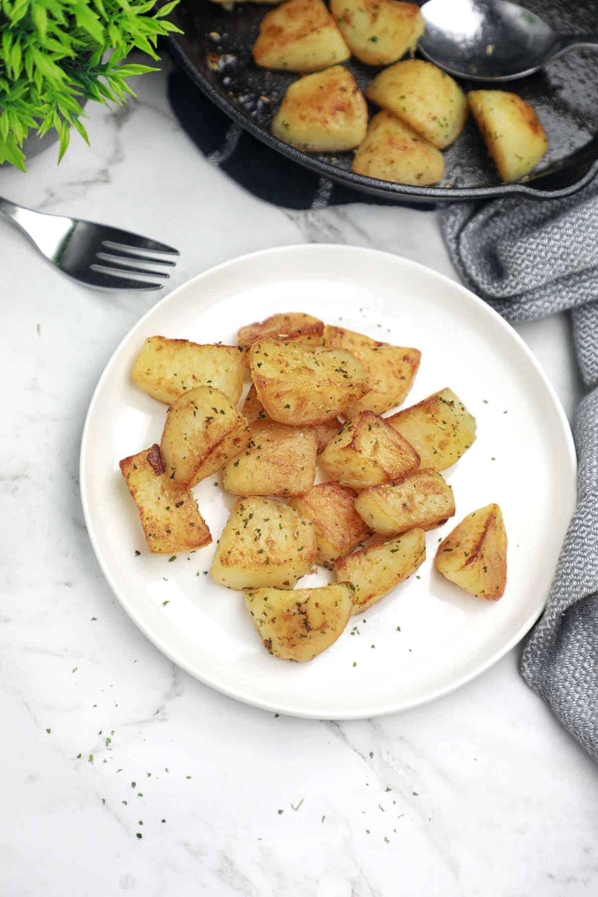some potatoes on a plate and some in the skillet.
