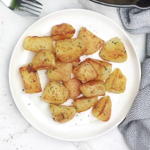 fried potatoes served on a white plate with skillet in background.