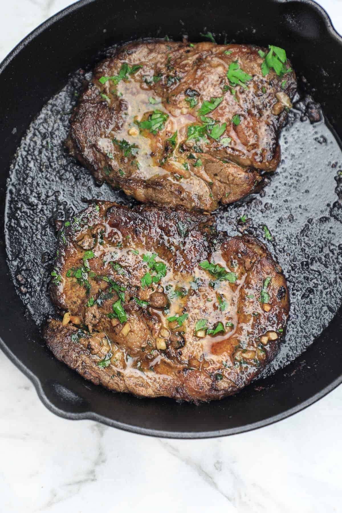 two pan fried steak in a skillet.