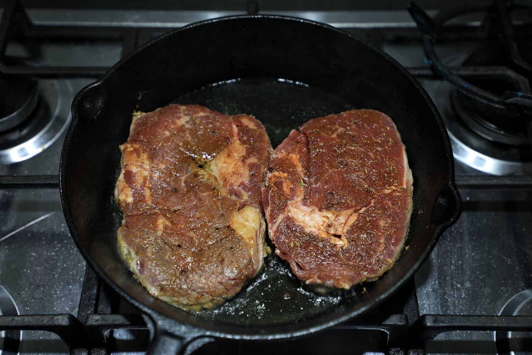 pan frying 2 steaks in a cast iron skillet.