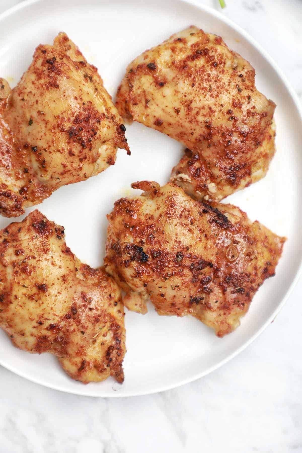 4 baked chicken thighs on a white plate.