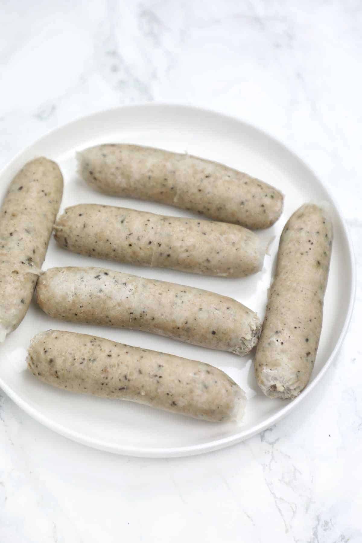 6 boiled sausages on a plate.