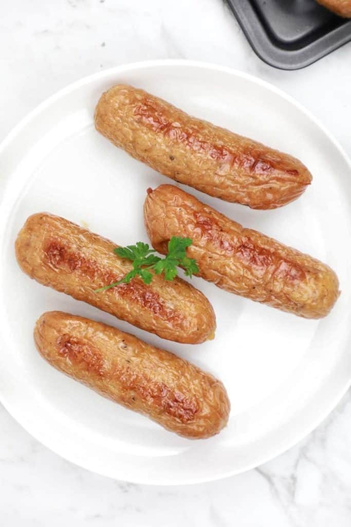 4 cooked sausages on a white plate.