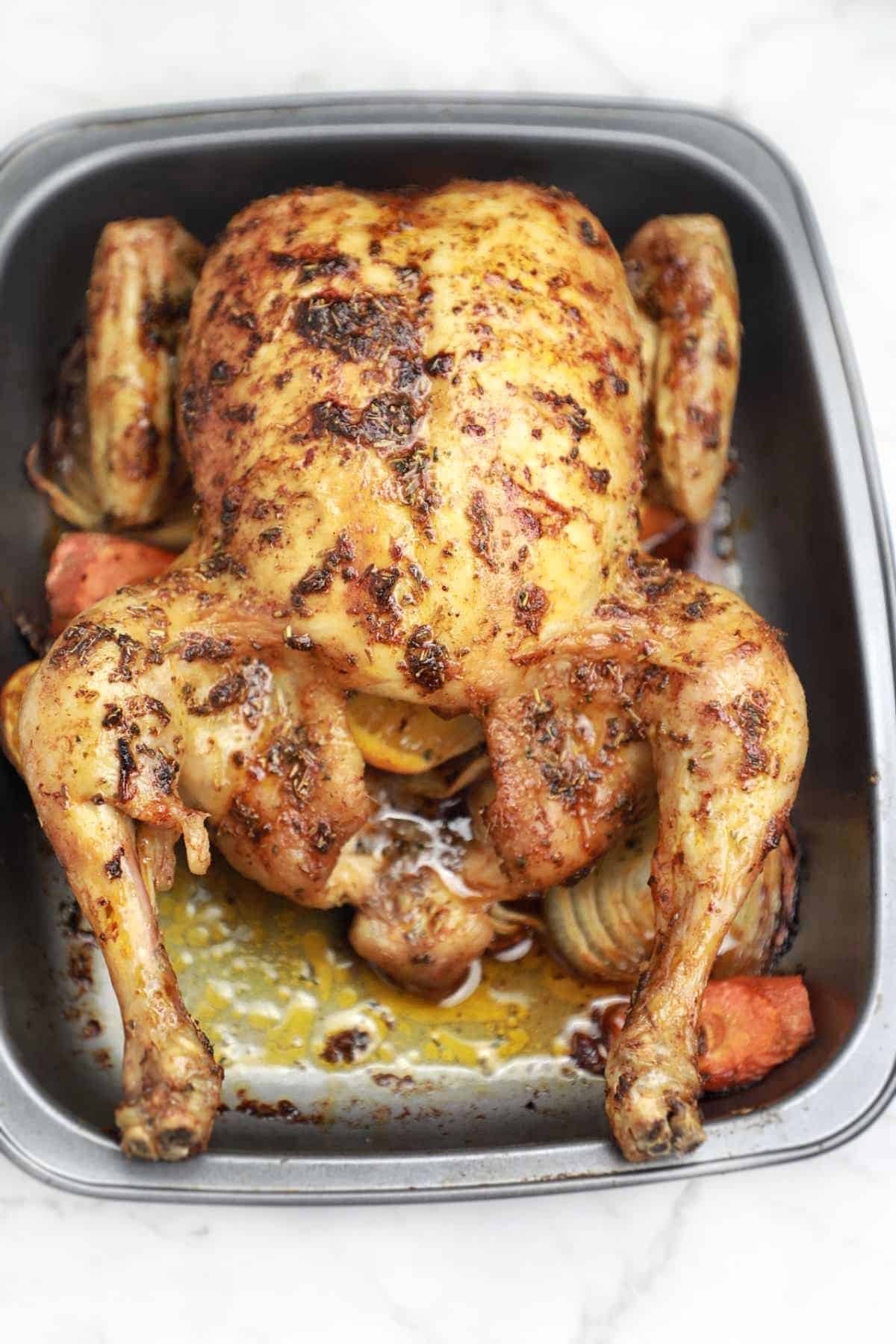 Whole roast chicken displayed in a grey baking dish.