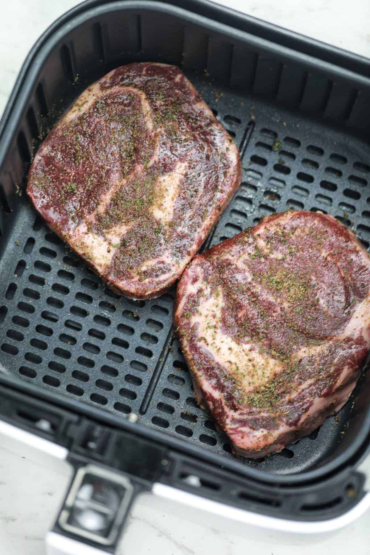 seasoned steaks in air fryer basket.