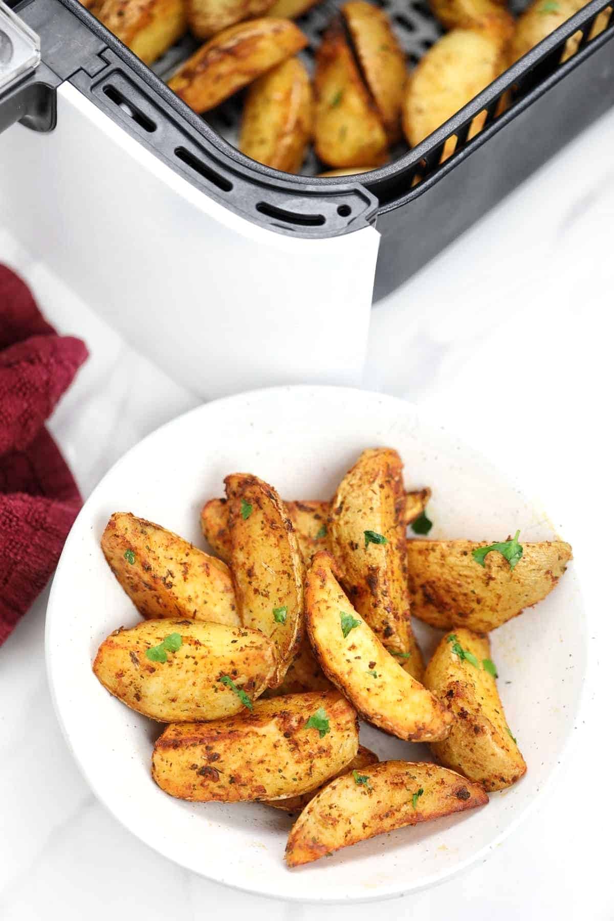 air fried potato wedges displayed on a plate and in the air fryer.