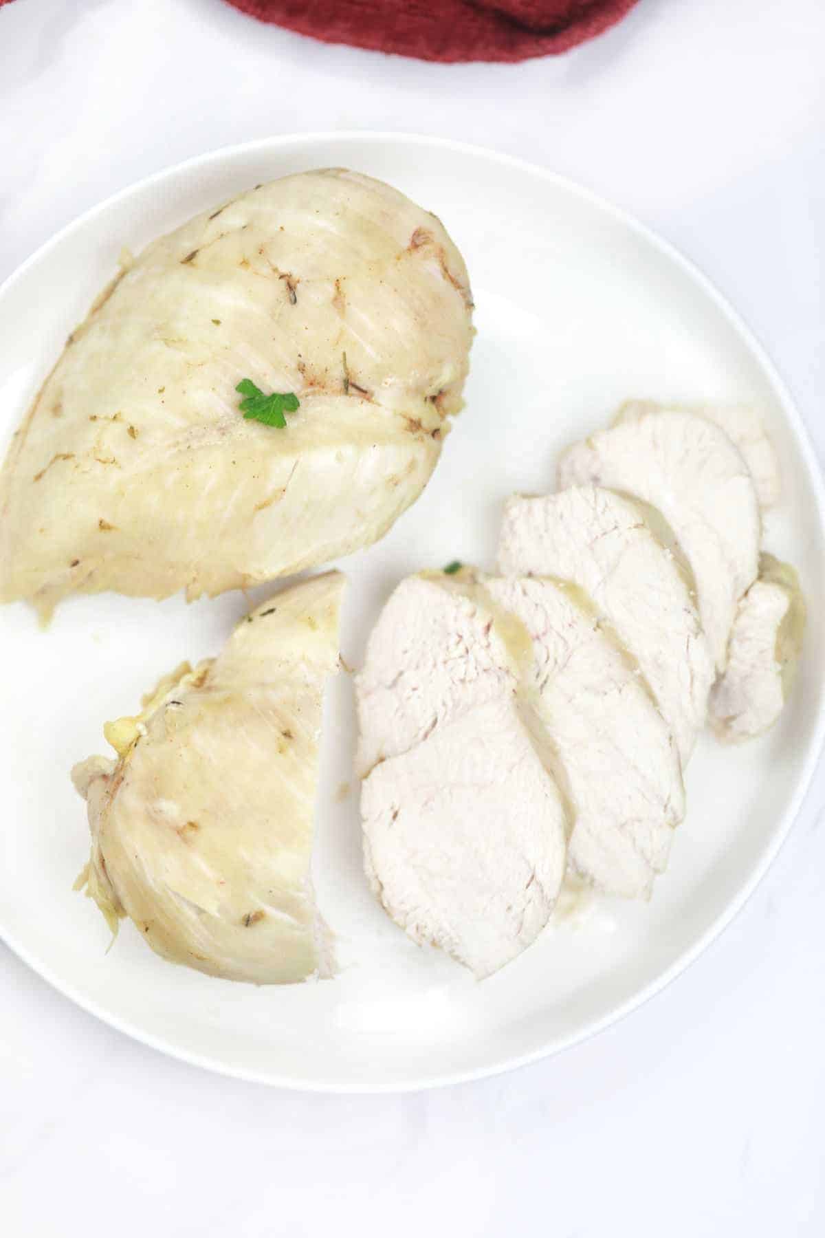 2 boiled chicken breast pieces on a plate with one sliced into smaller pieces.