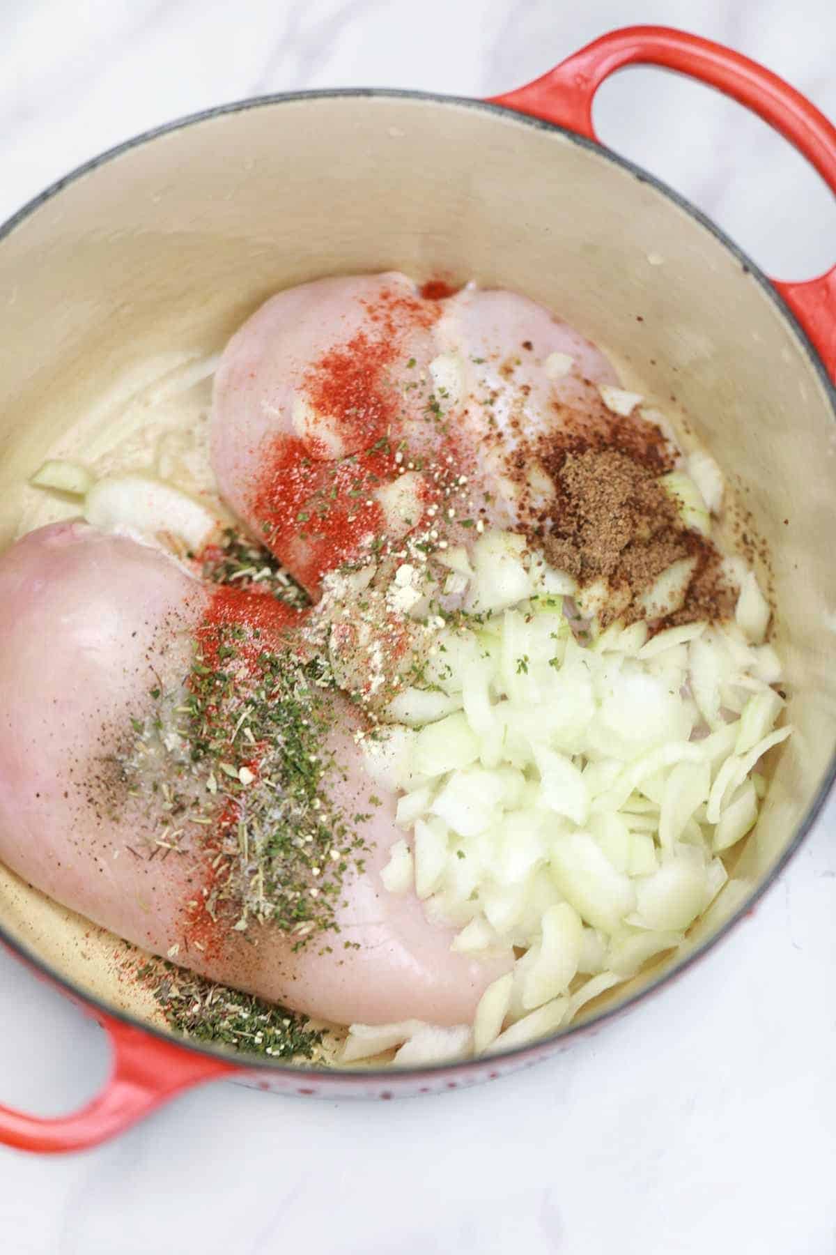 chicken, spices, and herbs in a red pot.