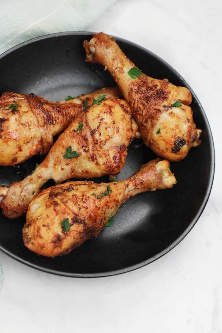 cooked marinated chicken drumsticks served on a black plate.