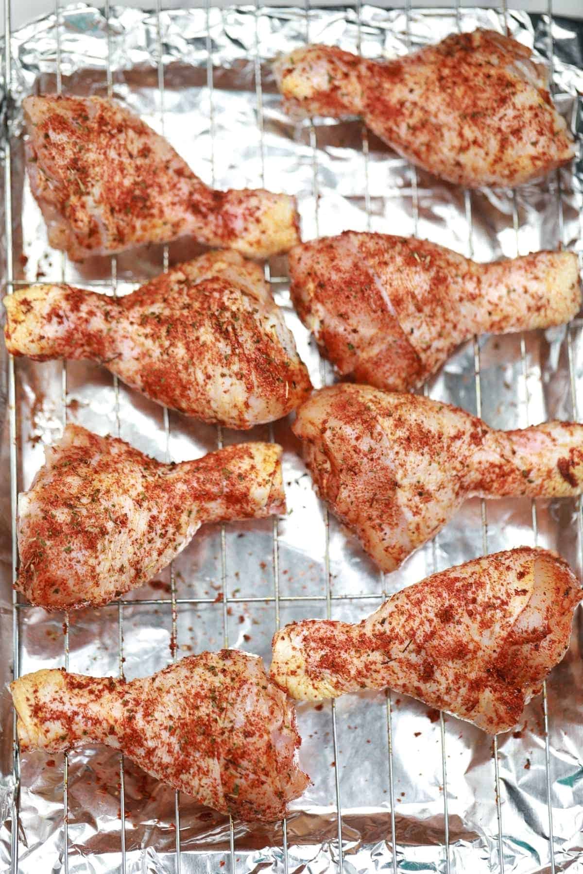 seasoned drumsticks on a rack covered baking tray.