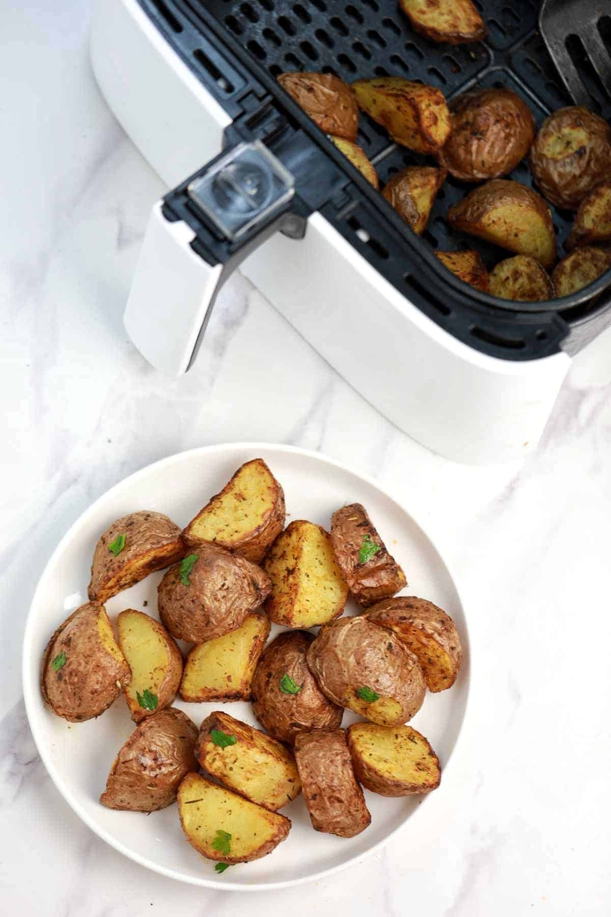 air fryer roasted red potatoes in a plate and in air fryer basket.