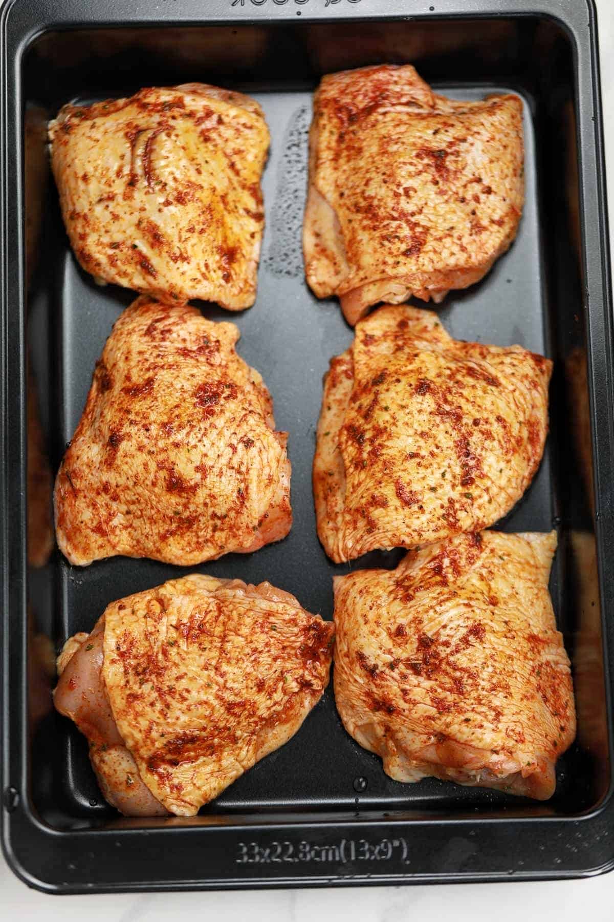 Seasoned chicken thighs on a baking pan.