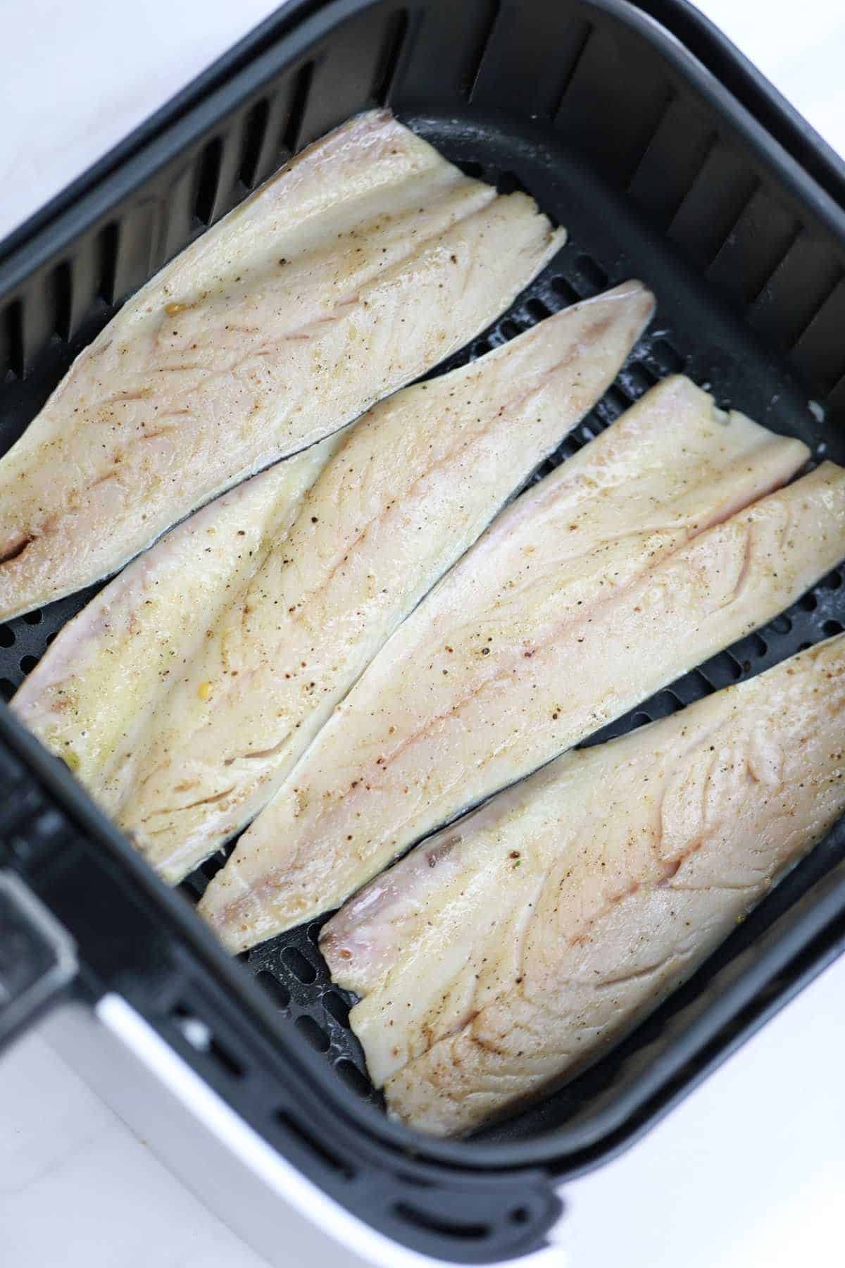 seasoned mackerel arranged in air fryer basket.