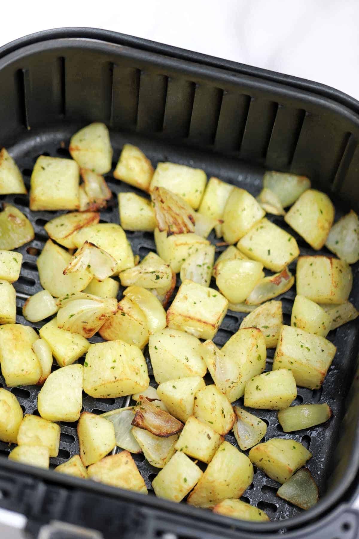 cooked potatoes and onions in air fryer basket.