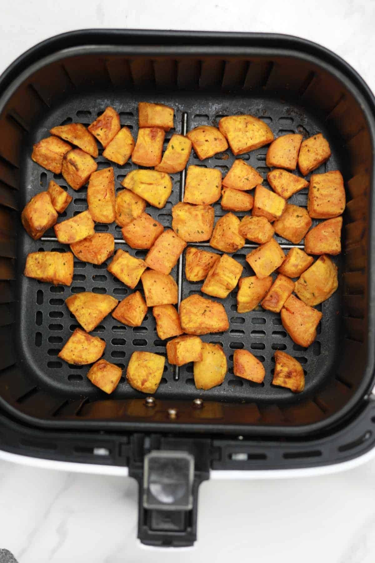 air fried sweet potato cubes in air fryer basket.