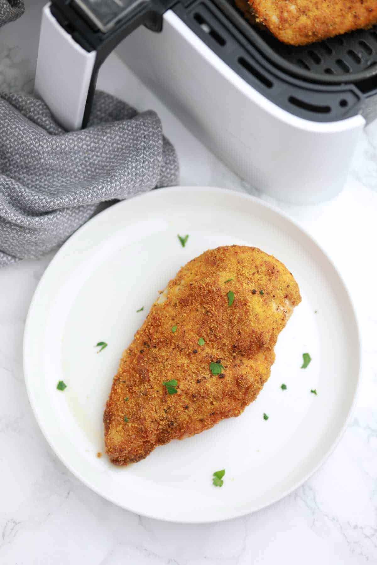 Breaded chicken breast in air fryer and on a white plate.
