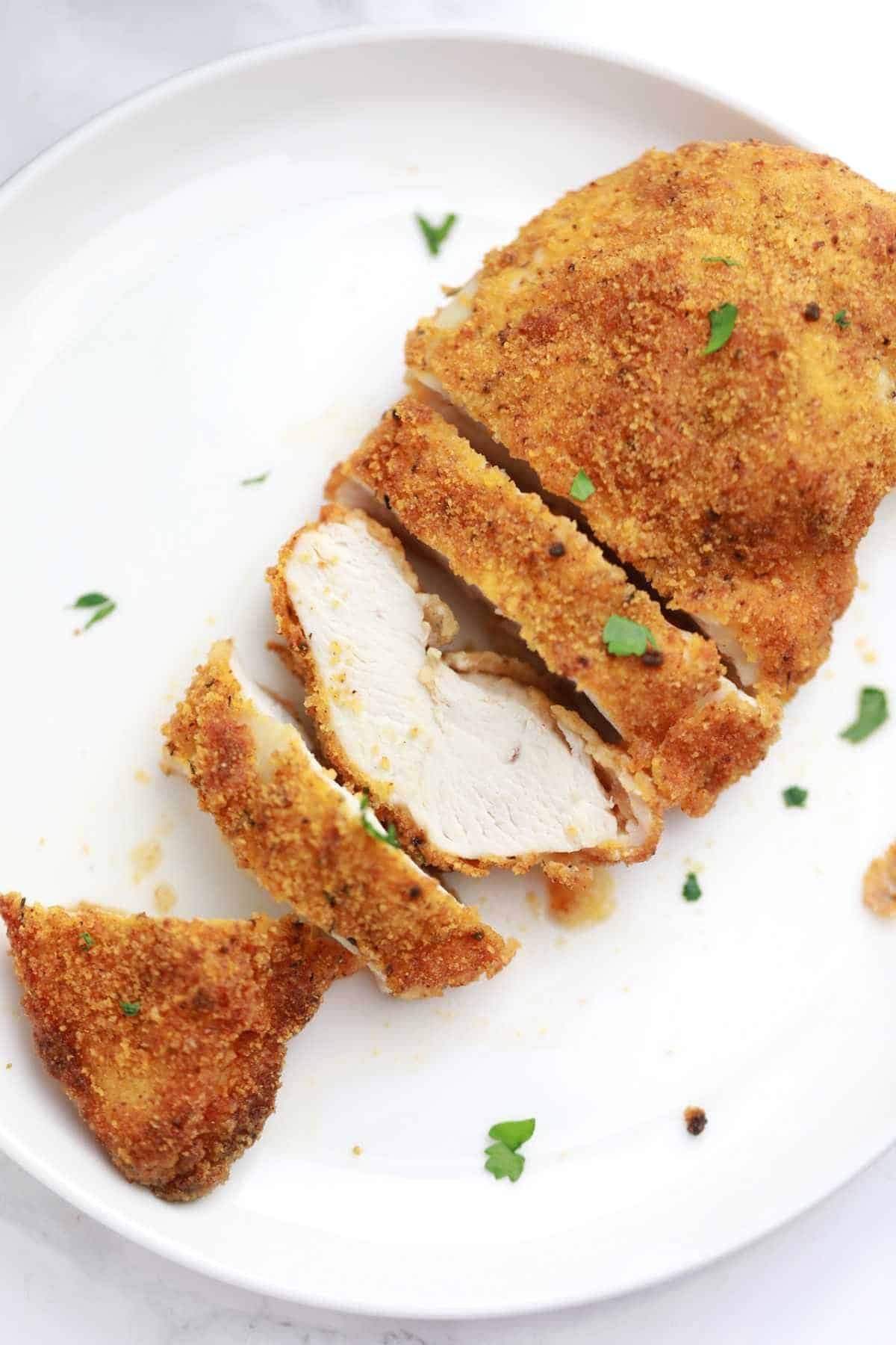 air fryer breaded chicken breast sliced and served on a white plate.