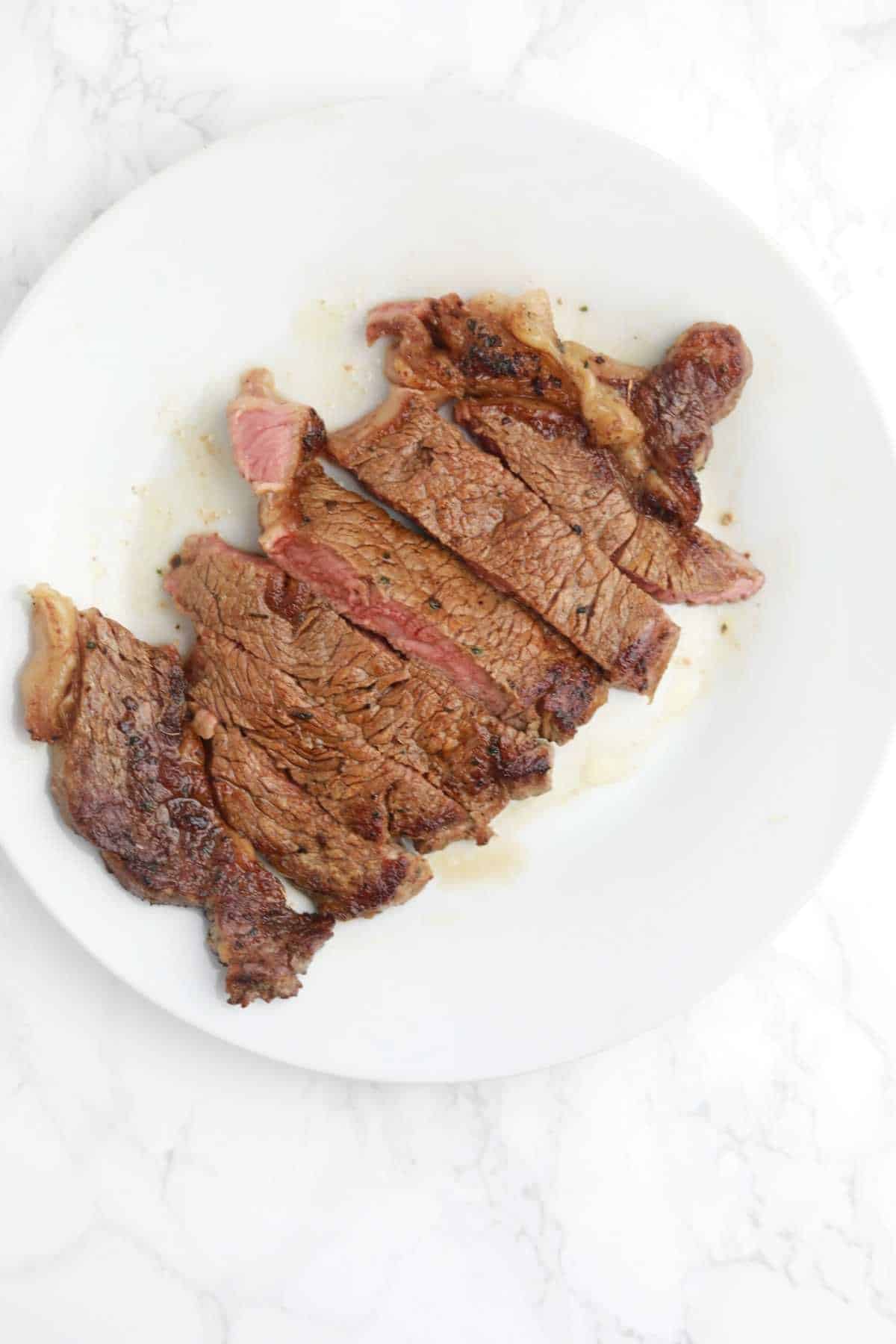 cooked and sliced steak on a white plate.