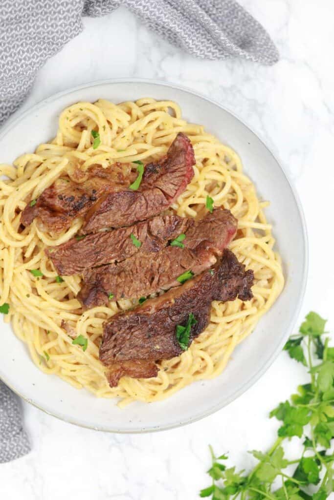 steak and pasta served and garnished with parsley.