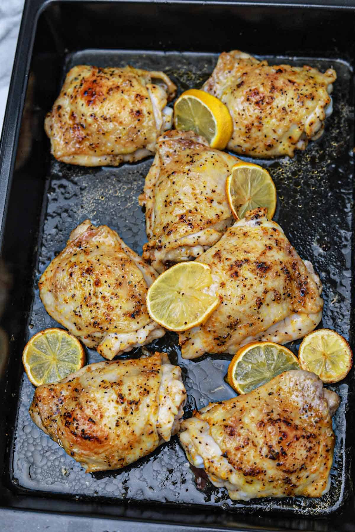 cooked lemon chicken thighs on a baking tray.