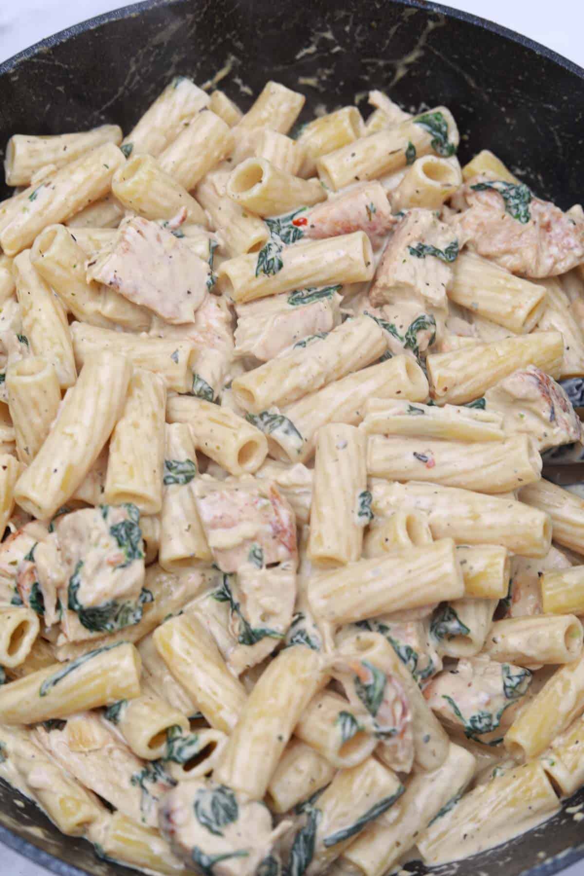 creamy chicken spinach pasta in a skillet.