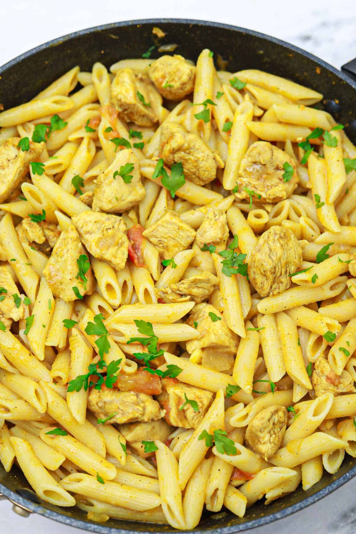 coconut chicken curry pasta in a pan garnished with coriander.