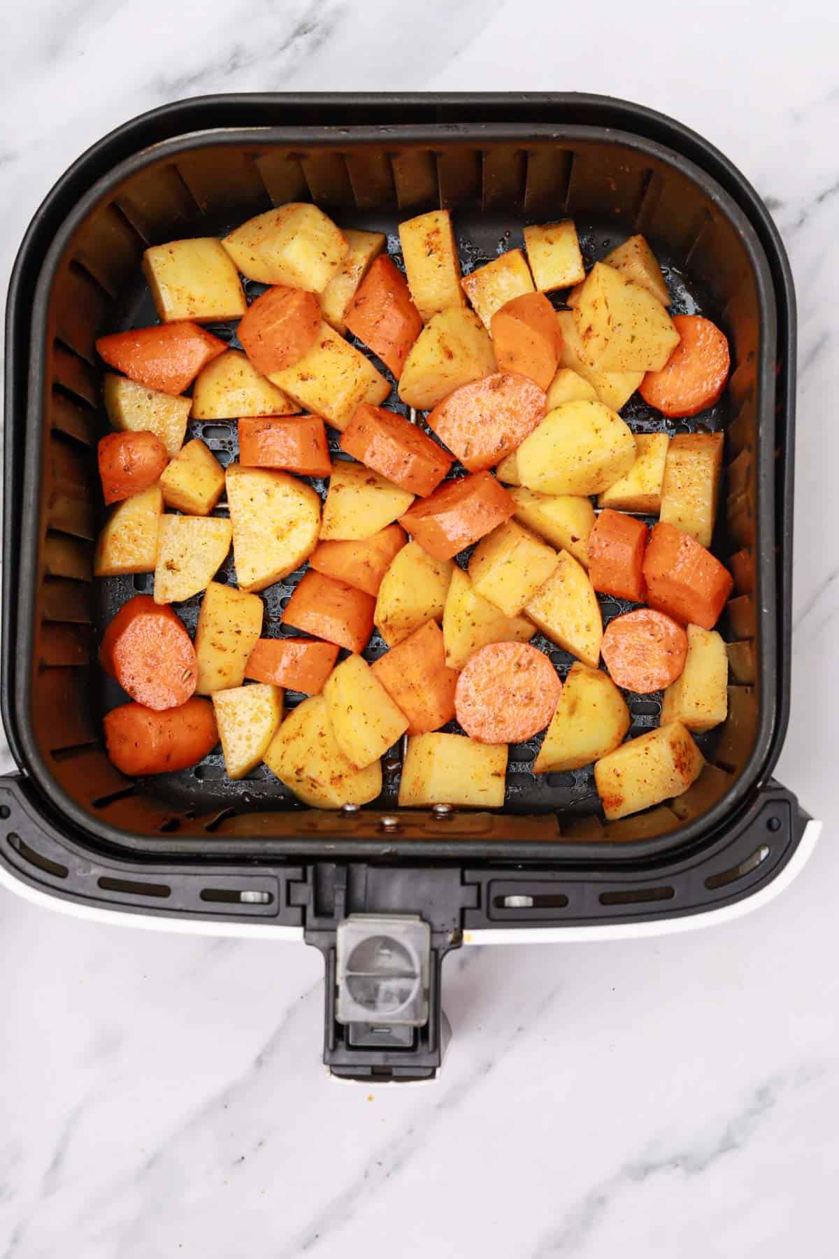 the seasoned potatoes and carrots in air fryer basket.