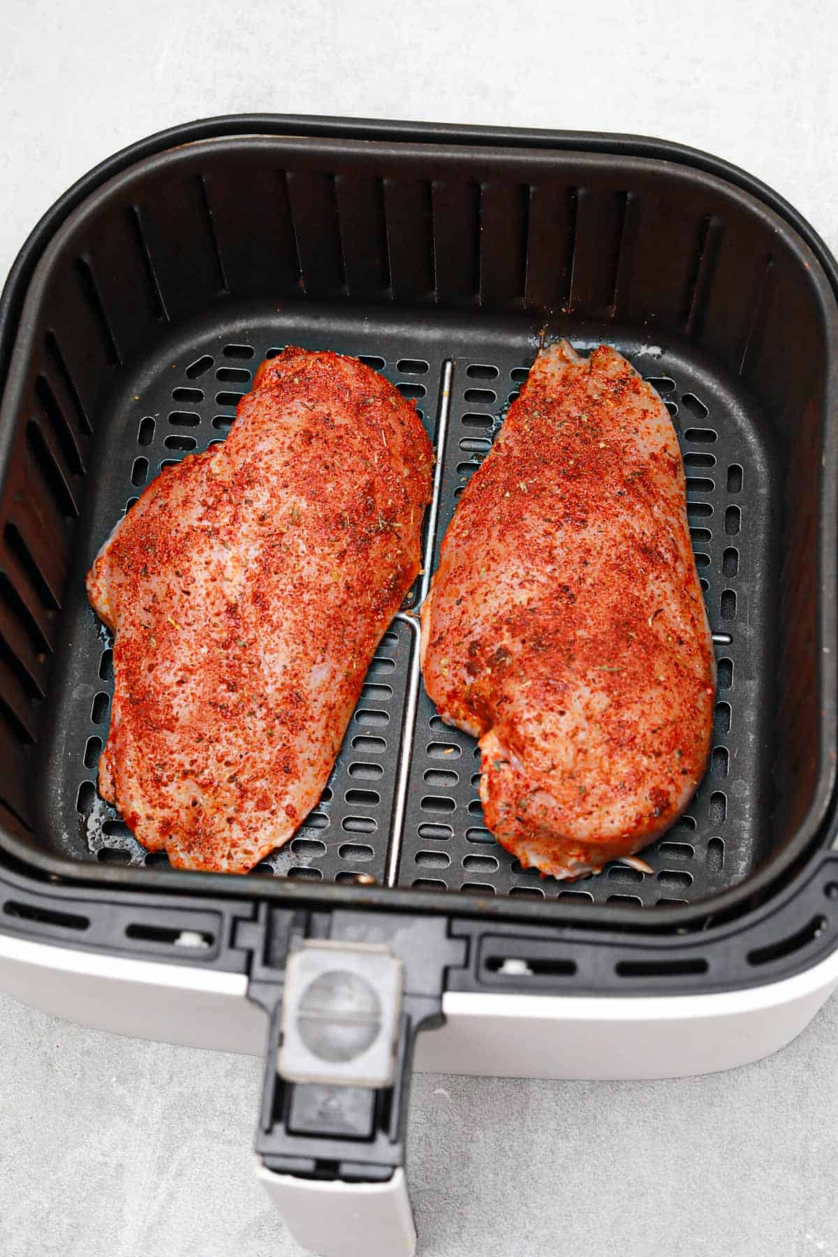 the seasoned chicken breasts in the air fryer basket.