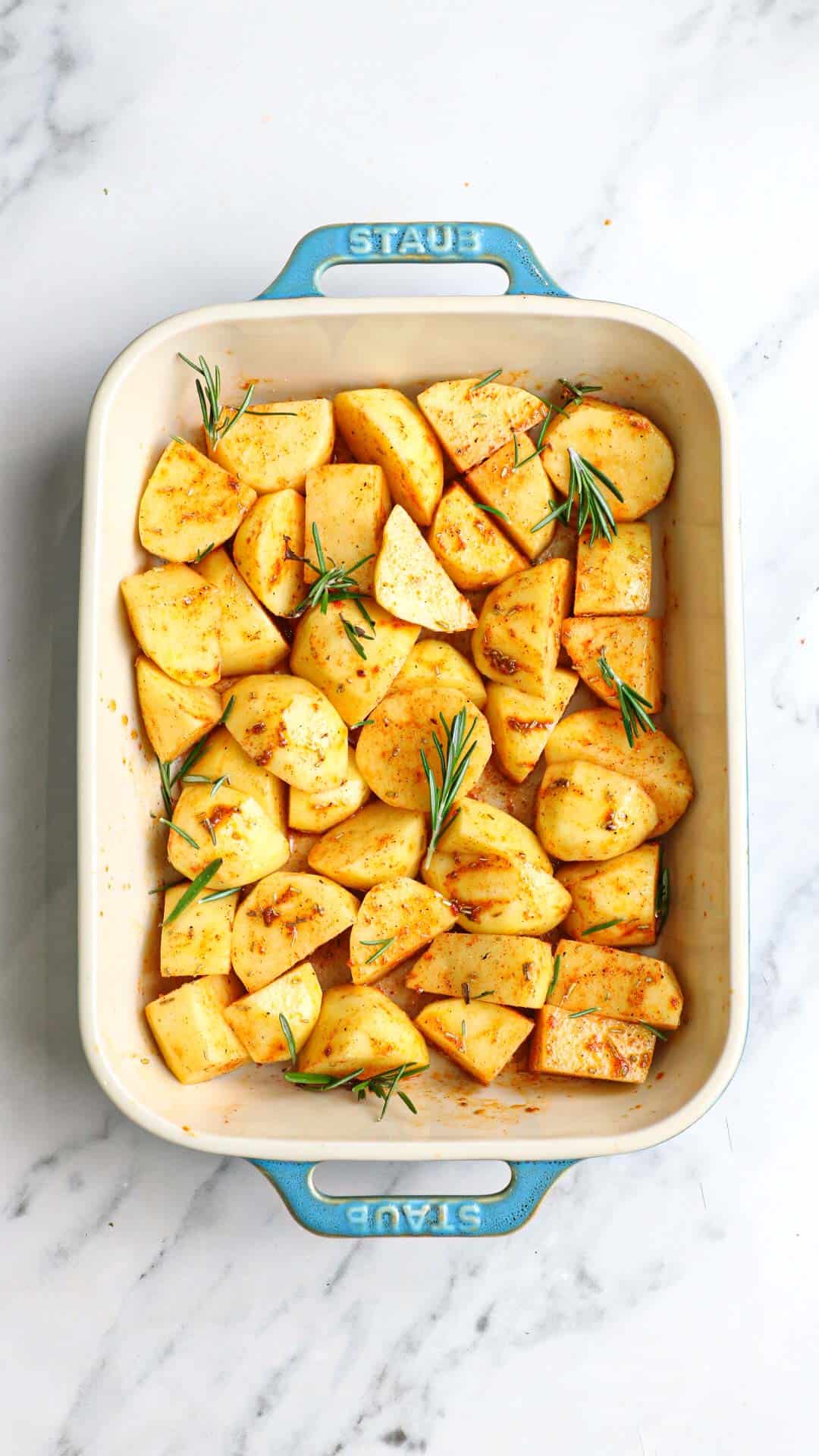 the seasoned potatoes in a baking dish garnished with fresh rosemary.